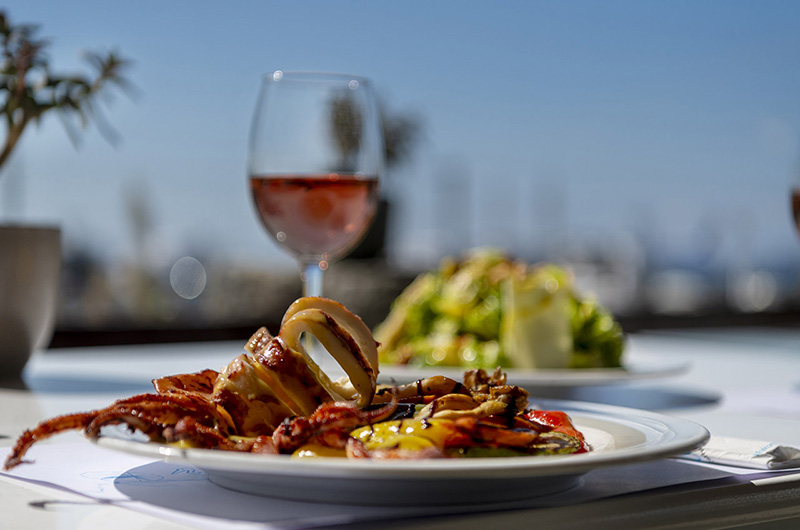 Seafood dish and wine at Molaraki Restaurant in Mykonos with blurred Mykonos port view in the background 02-molaraki-restaurant-mykonos-seafood-dish-wine-port-view