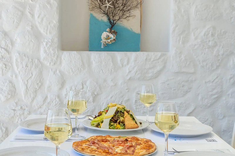 Indoor dining at Molaraki Restaurant in Mykonos with pizza, fresh salad and wine served on a white Cycladic setting 06-molaraki-restaurant-mykonos-indoor-dining-pizza-salad-wine